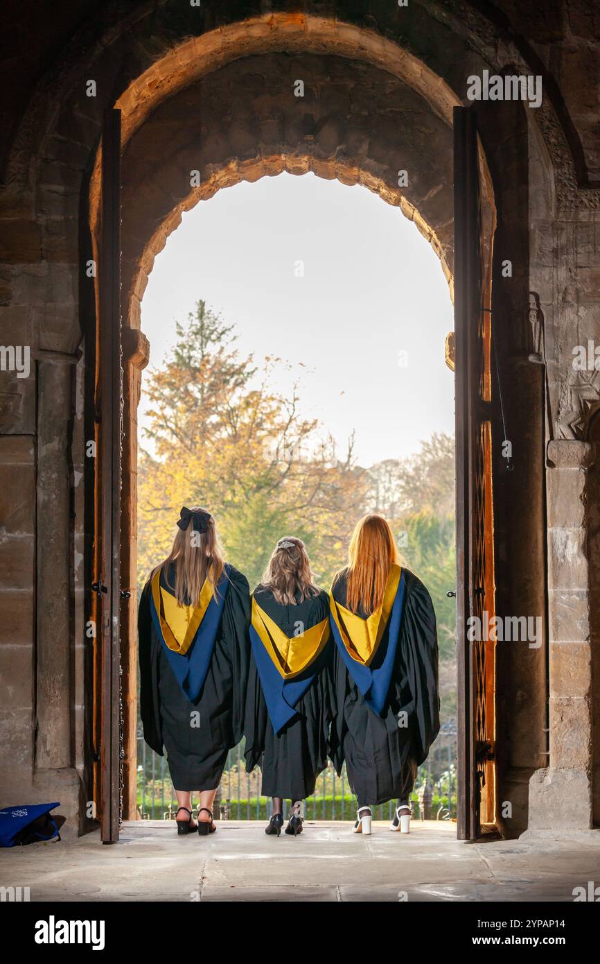 Una veduta posteriore di tre studentesse in piedi all'ingresso di una chiesa con abiti da laurea Foto Stock