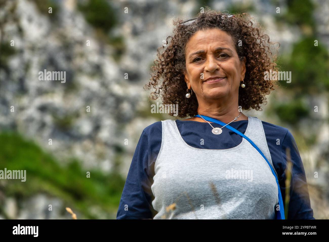 Una bella donna sudamericana, di mezza età con capelli ricci, dà un tocco di sorriso timido Foto Stock