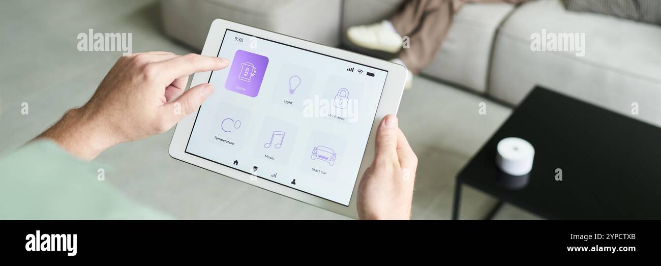 Persona che utilizza un tablet per controllare il sistema di automazione domestica mentre è seduto sul divano in un salotto moderno. Visualizzazione di icone diverse per vari dispositivi domestici Foto Stock