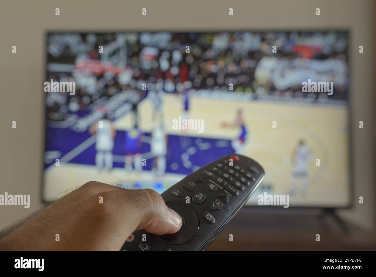 11 maggio 2024, Brasile. In questa illustrazione fotografica, una mano che tiene un telecomando TV davanti alla a che trasmette una partita di basket in TV Foto Stock