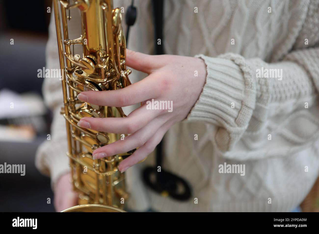 Adolescente che suona il sassofono in salotto a distanza ravvicinata di mani e dita sui tasti Foto Stock