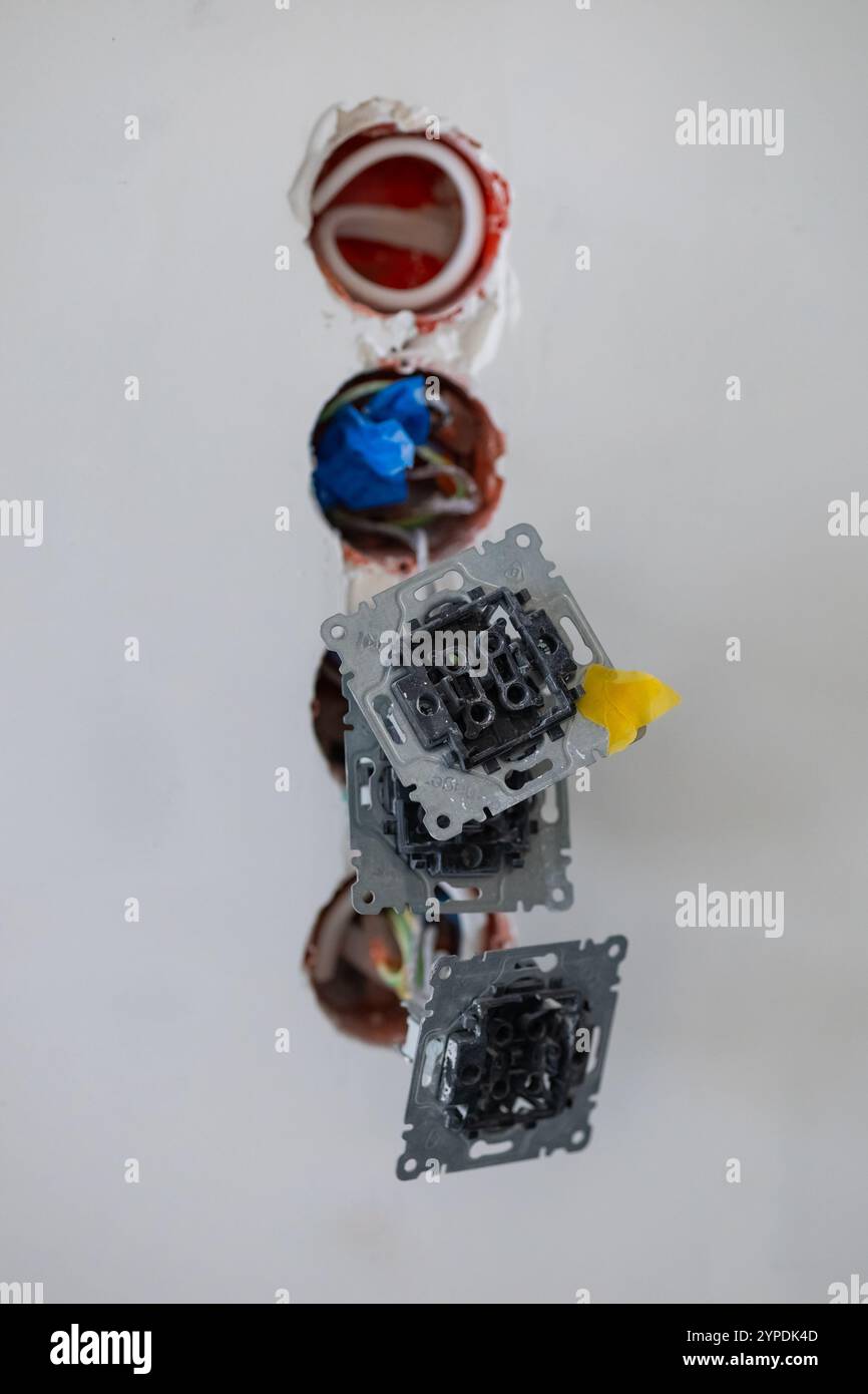 Primo piano dell'installazione di cablaggi elettrici in una parete durante la costruzione o la ristrutturazione, mostrando fili esposti, nastro protettivo e telai di prese metalliche Foto Stock