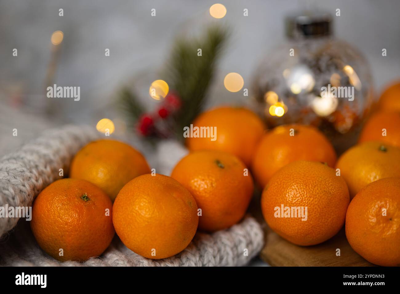 Mandarini freschi su un'accogliente coperta di lana con luci bokeh natalizie e decorazioni natalizie sullo sfondo. Vacanze invernali e frutta di stagione Foto Stock