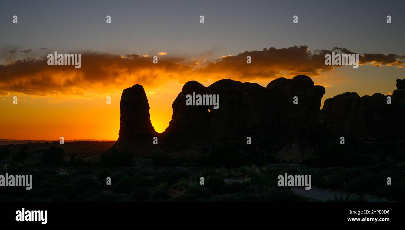 Il bagliore arancione del sole che tramonta dietro la formazione rocciosa nel Parco Nazionale degli Arches Foto Stock