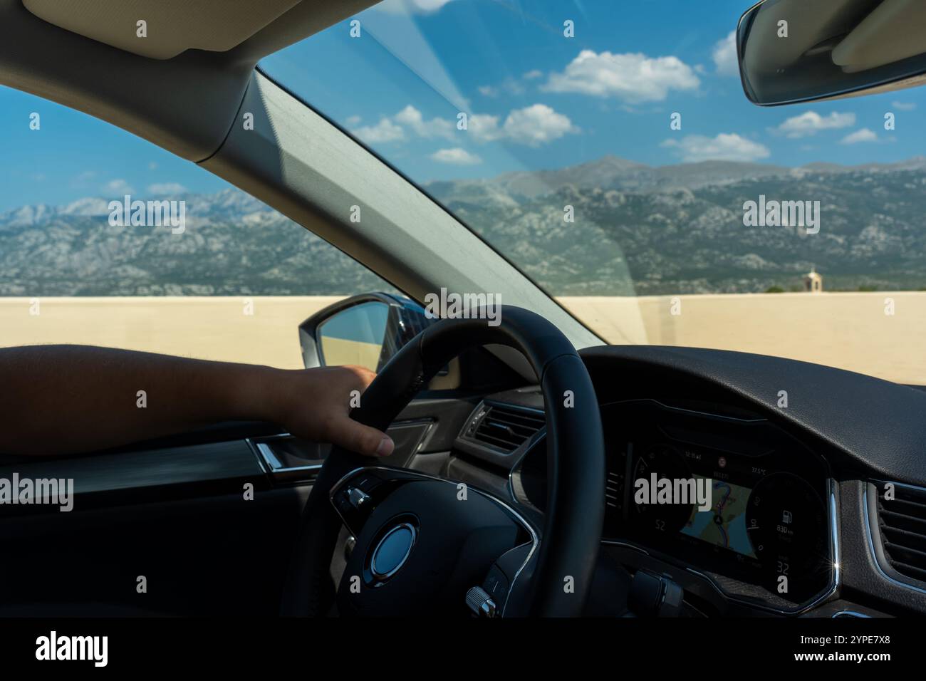 Vista interna dell'auto che guida su un'autostrada con una panoramica catena montuosa sullo sfondo sotto il cielo azzurro. Concetto di viaggi su strada, viaggi di avventura, Foto Stock