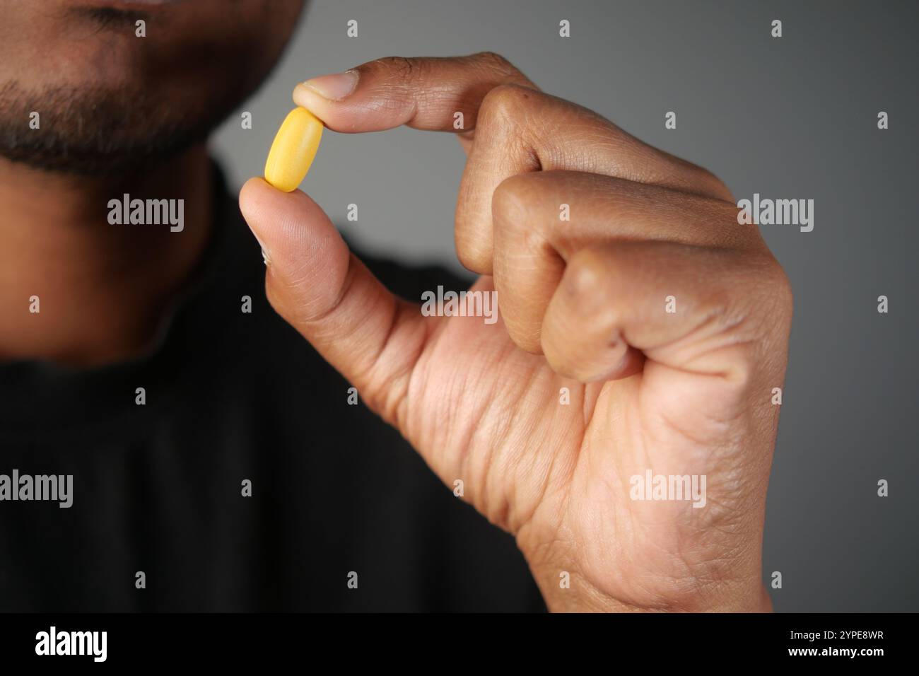 Un individuo sta tenendo in mano una capsula gialla di integratore alimentare Foto Stock