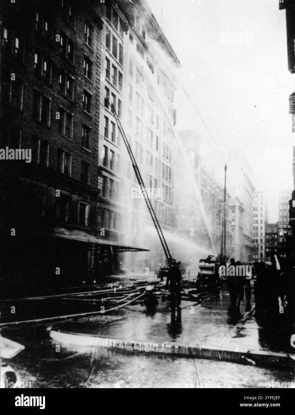 I vigili del fuoco spruzzano acqua sull'edificio Asch in fiamme durante l'incendio della fabbrica Triangle Shirtwaist del 25 marzo 1911. Il Triangle Shirtwaist Factory Fire è stato uno dei peggiori incidenti industriali nella storia degli Stati Uniti. E' scoppiato un incendio al decimo piano dell'Asch Building. Le uscite antincendio erano chiuse a chiave, l'uscita antincendio inadeguata e le scale dei motori antincendio non erano abbastanza lunghe. 146 persone furono uccise, di cui 62 saltarono alla morte per evitare le fiamme. Questa foto mostra chiaramente che le scale raggiungevano solo il 6° piano e che l'incendio era il 10°. Foto Stock