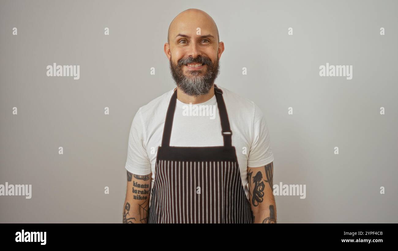 Bell'ispanico con barba e tatuaggi che indossano un grembiule che sorride con sicurezza su uno sfondo bianco isolato Foto Stock