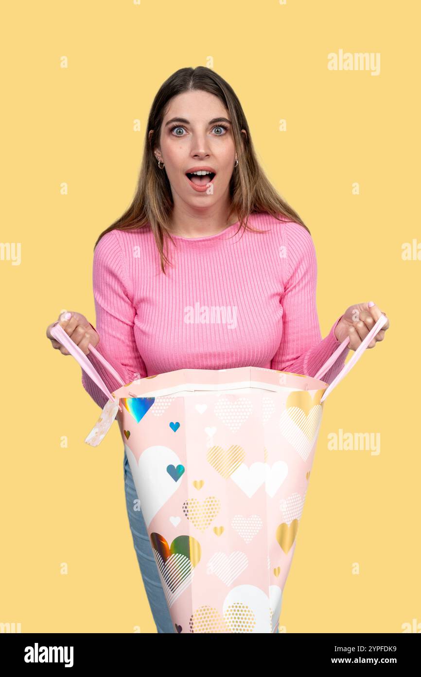 Foto in studio di una giovane donna sorpreso che apre una borsa regalo di san valentino con forme a cuore e che esprime stupore Foto Stock