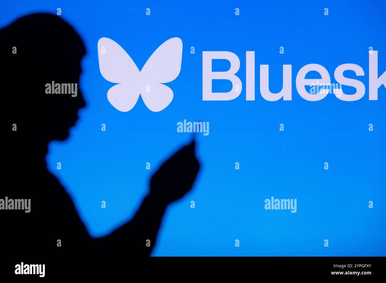 NEW YORK, USA, 30 OTTOBRE 2024: Uomo che passa del tempo online sulla piattaforma sociale Bluesky. Silhouette e logo Bluesky sullo sfondo Foto Stock