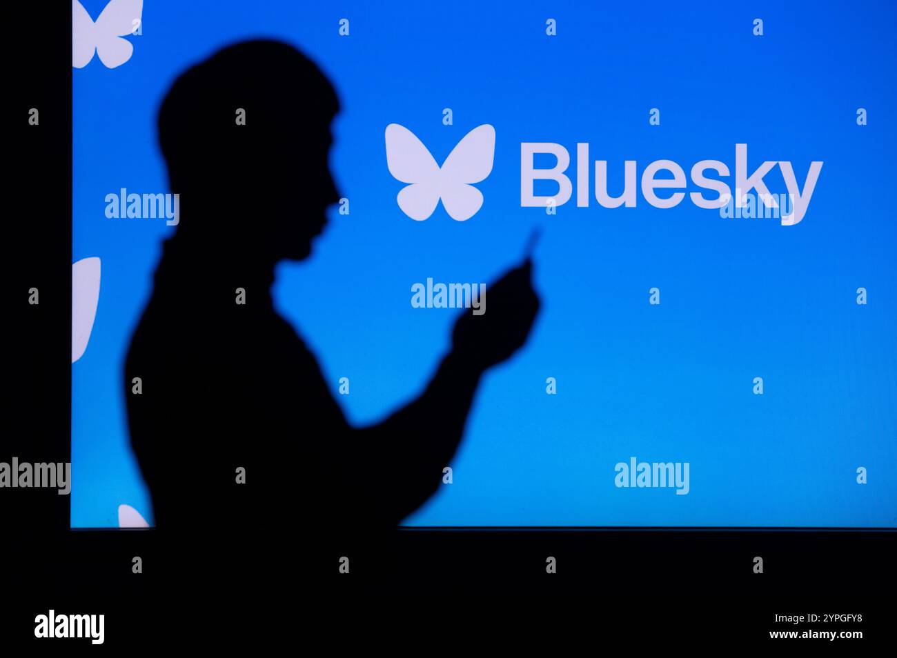 NEW YORK, USA, 30 OTTOBRE 2024: Young Asian Man Exploring Bluesky's Social Platform. Silhouette di giovane uomo su smartphone e logo aziendale sul retro Foto Stock