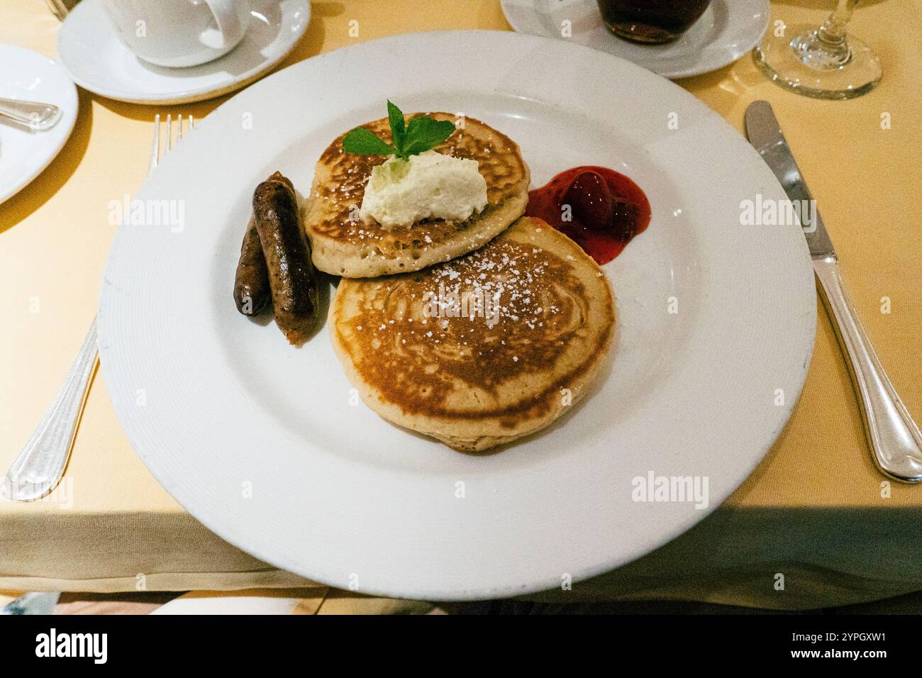 Soffici pancake al siero di latte conditi con burro fondente e un rametto di menta, abbinati a salsicce grigliate e un cucchiaio di condimento di fragole Foto Stock