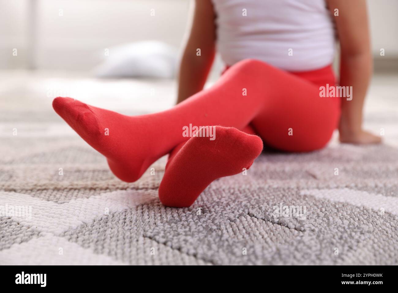 Bambino in collant rossi seduto sul pavimento di casa, primo piano Foto Stock