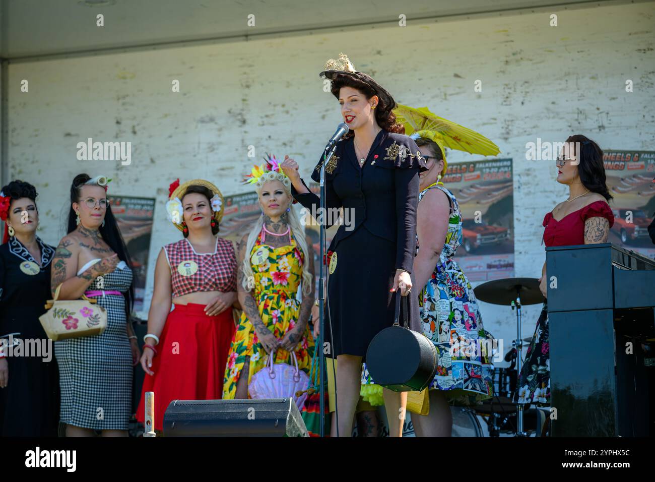 La vivace moda vintage prende vita mentre un gruppo di donne mette in mostra con fiducia i loro stili unici sul palco in un vivace festival locale, coinvolgendo l'aud Foto Stock