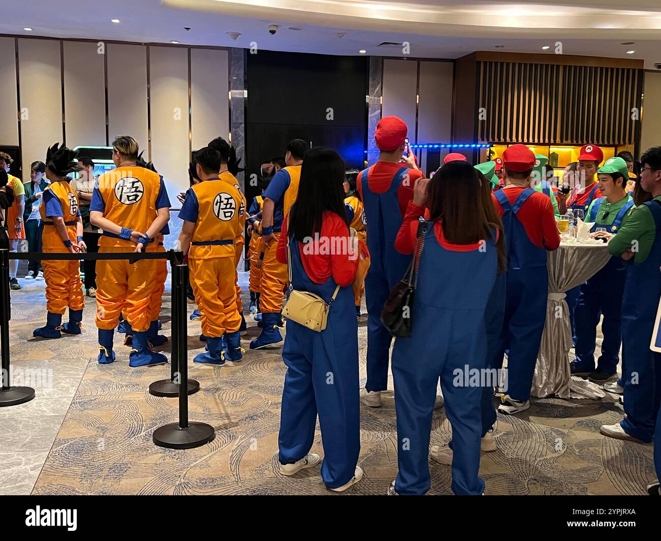 Interno della sala da ballo pieno di persone vestite con il costume Dragon Ball Goku, un altro vestito di gruppo con l'aspetto dei personaggi a tema Super Mario. Singapore - Immagine stock catturata con smartphone