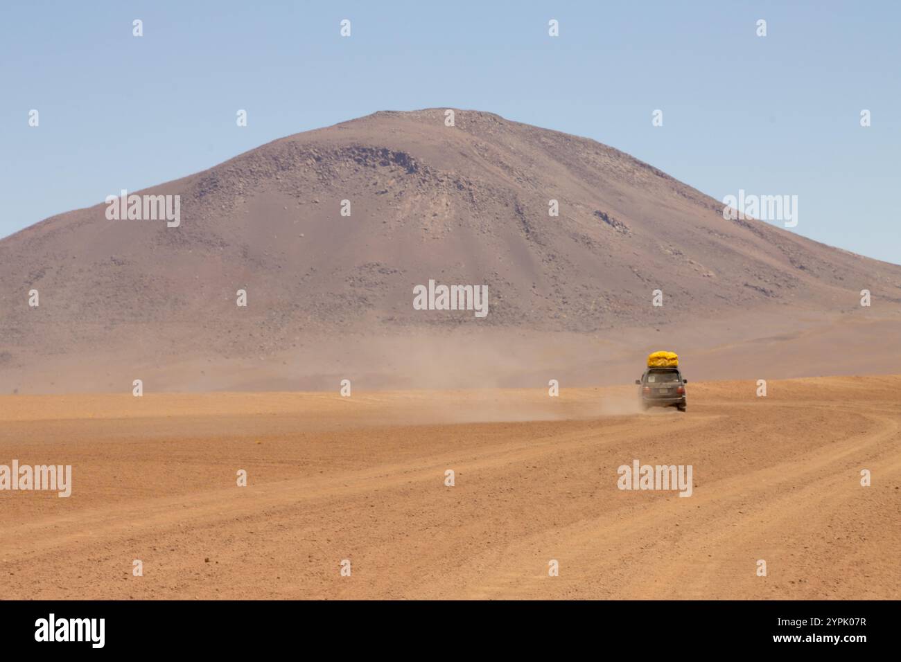 Un veicolo fuoristrada guida nel vasto paesaggio desertico dell'Altiplano boliviano, circondato da aride pianure e maestose catene montuose Foto Stock