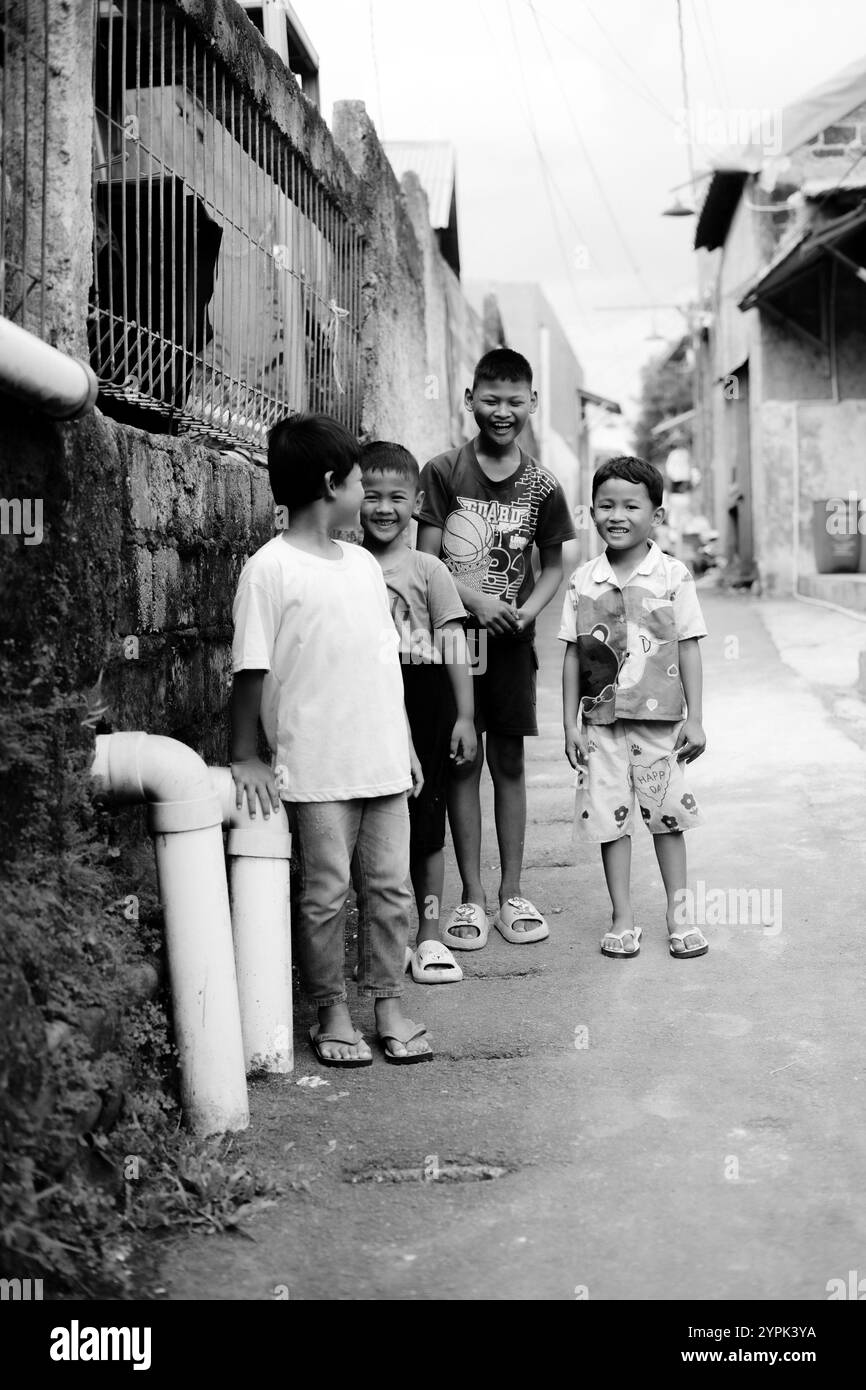 Bogor, 24 novembre 2024. Quattro bambini piccoli in piedi insieme in un vicolo stretto, sorridenti e guardano intorno in un vivace ambiente del quartiere Foto Stock