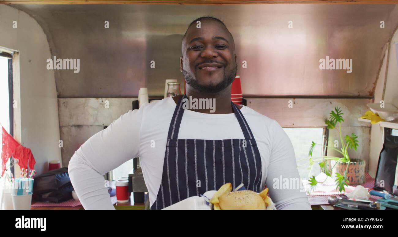 Sorridente imprenditore afroamericano che tiene un pasto da asporto in un furgone alimentare Foto Stock