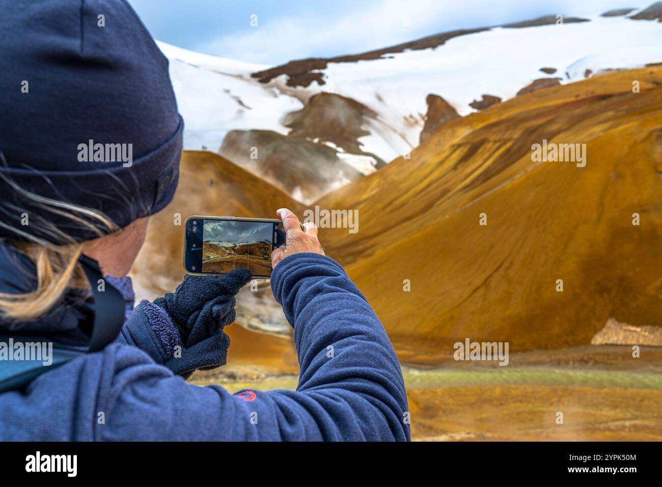 Una donna con un cappello blu fotografa i pendii fumosi e nebbiosi del vulcano Laki in Islanda, catturando le meraviglie geotermiche e l'aspra bellezza vulcanica. Foto Stock