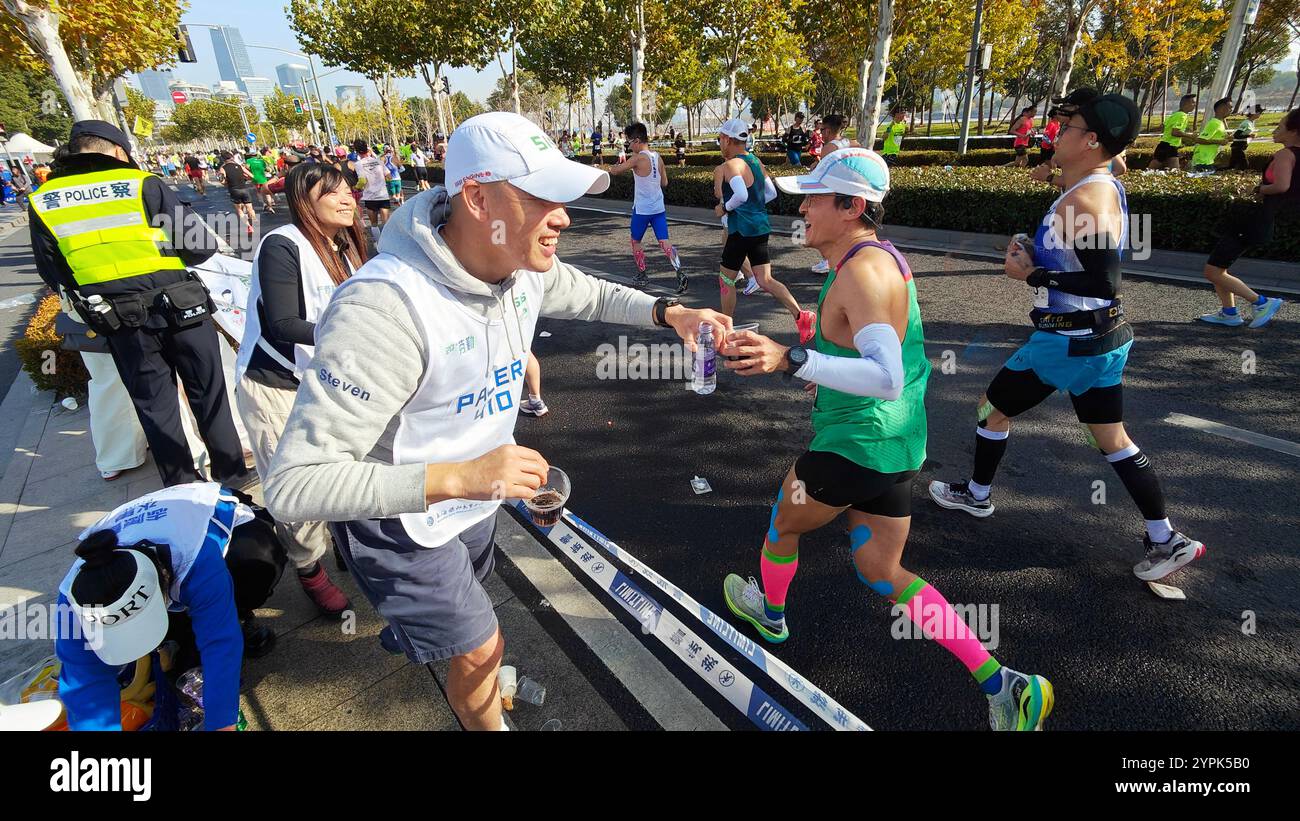 SHANGHAI, CINA - 1° DICEMBRE 2024 - i volontari forniscono acqua, banane e altre fonti di energia ai corridori durante la maratona di Shanghai a Shanghai, Foto Stock