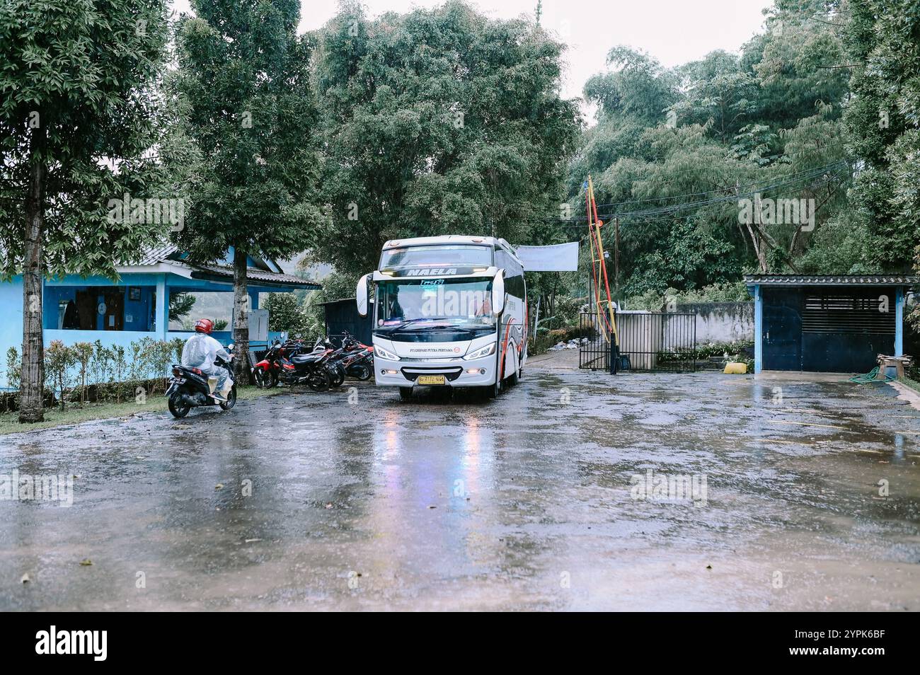 Bogor, 18 novembre 2024. Un autobus rosso entra nell'area parcheggio di una villa, circondato da vegetazione lussureggiante e dintorni panoramici Foto Stock