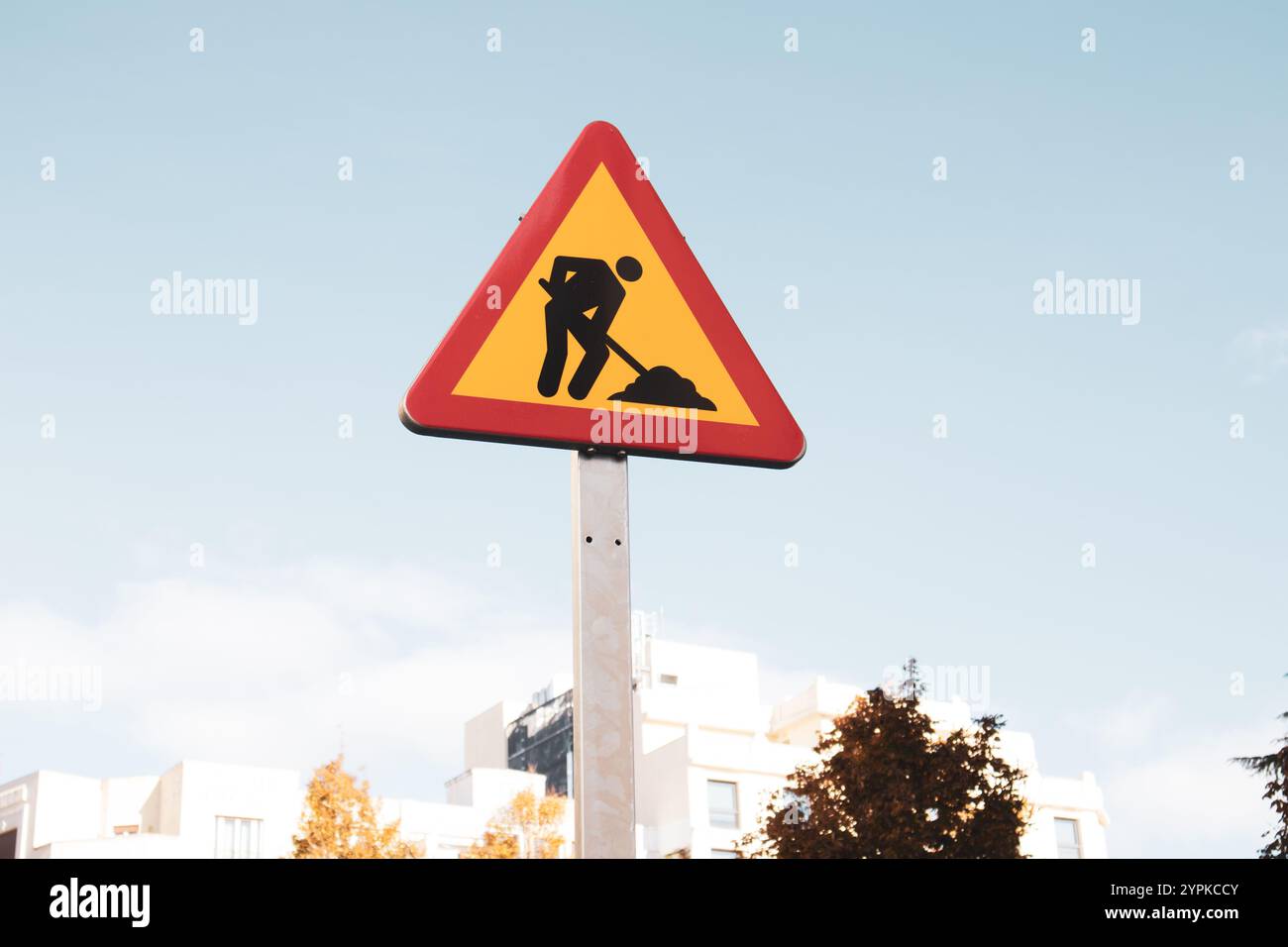 Cartellino triangolare rosso giallo dei lavori stradali su una strada della città contro il cielo blu. Icona di costruzione temporanea in ambiente urbano. Lavori in corso. L'uomo sta lavorando Foto Stock