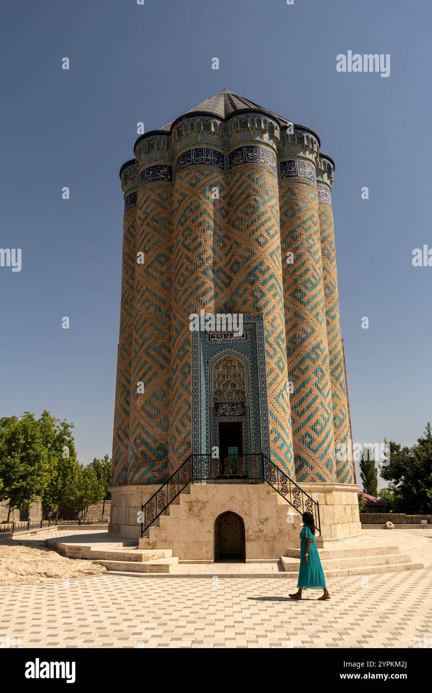 Una donna cammina vicino allo storico Mausoleo di Garabaghlar a Nakhchivan, Azerbaigian. La luminosa giornata di sole mette in risalto l'intricata architettura e la serena Foto Stock
