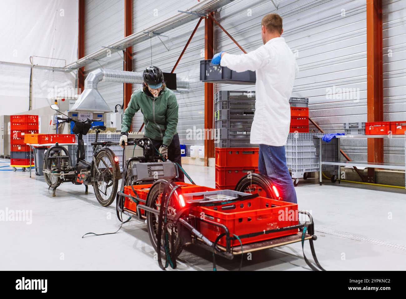 PRODUZIONE - 26 novembre 2024, Francia, Straßburg: Quentin Bagy (cappotto bianco) aiuta un corriere di biciclette (in verde) a scaricare un rimorchio di carico con container sporchi. L'azienda francese Uzaje desidera attirare clienti tedeschi per la pulizia degli imballaggi riutilizzabili presso il suo nuovo centro di lavaggio. Foto: Philipp von Ditfurth/dpa Foto Stock