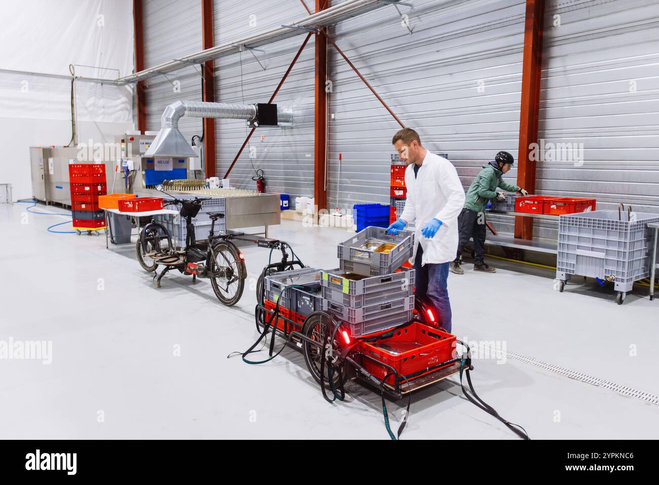 PRODUZIONE - 26 novembre 2024, Francia, Straßburg: Quentin Bagy (cappotto bianco) aiuta un corriere di biciclette (in verde) a scaricare un rimorchio di carico con container sporchi. L'azienda francese Uzaje desidera attirare clienti tedeschi per la pulizia degli imballaggi riutilizzabili presso il suo nuovo centro di lavaggio. Foto: Philipp von Ditfurth/dpa Foto Stock