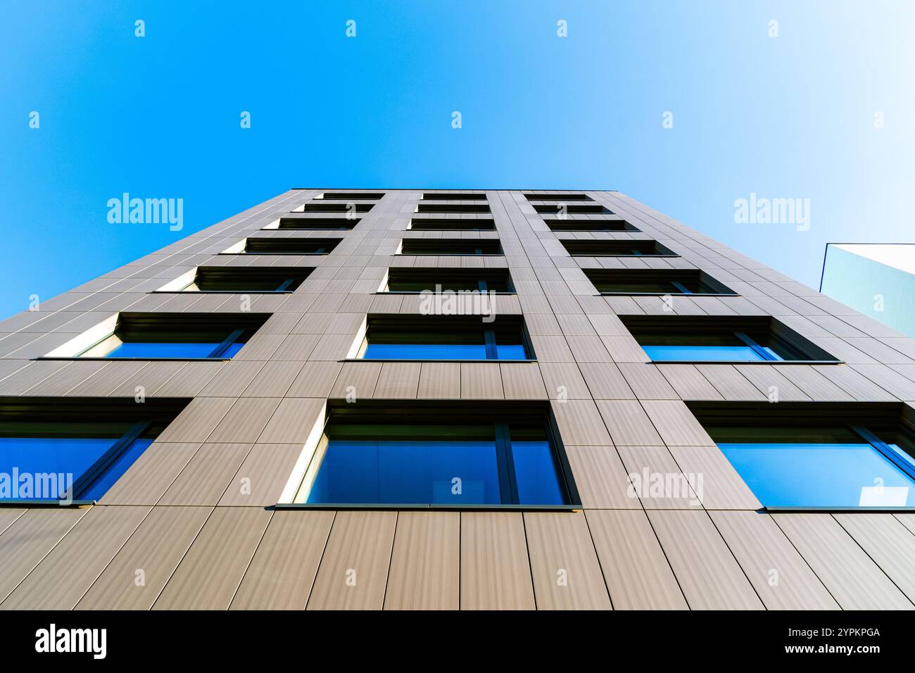 Prospettiva verticale di un edificio moderno con finestre riflettenti contro un cielo blu chiaro Foto Stock