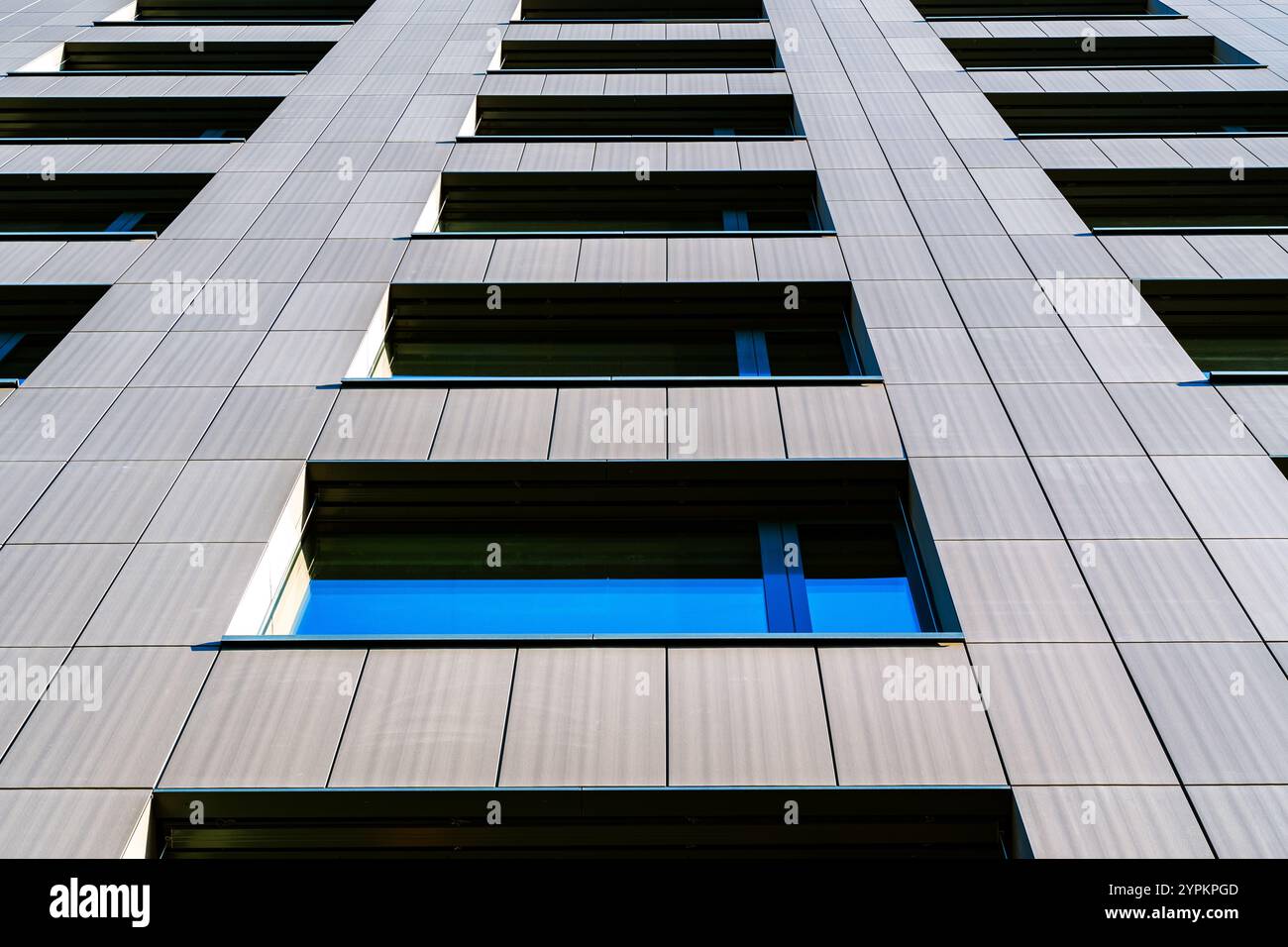 Prospettiva verticale di un edificio moderno con finestre riflettenti contro un cielo blu chiaro Foto Stock