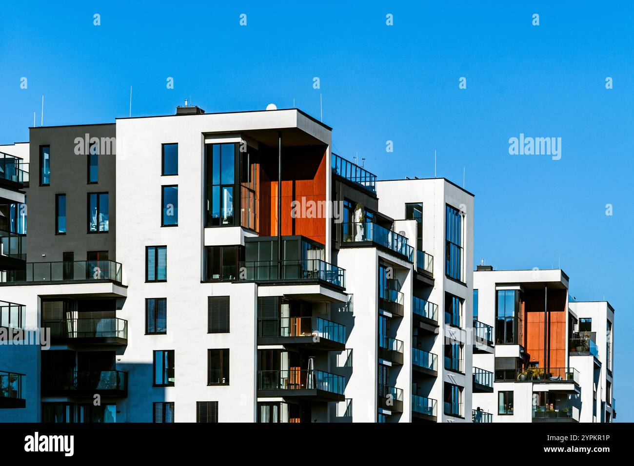 Edifici residenziali contemporanei con balconi moderni, facciate in mattoni e riflessi sotto un cielo limpido Foto Stock