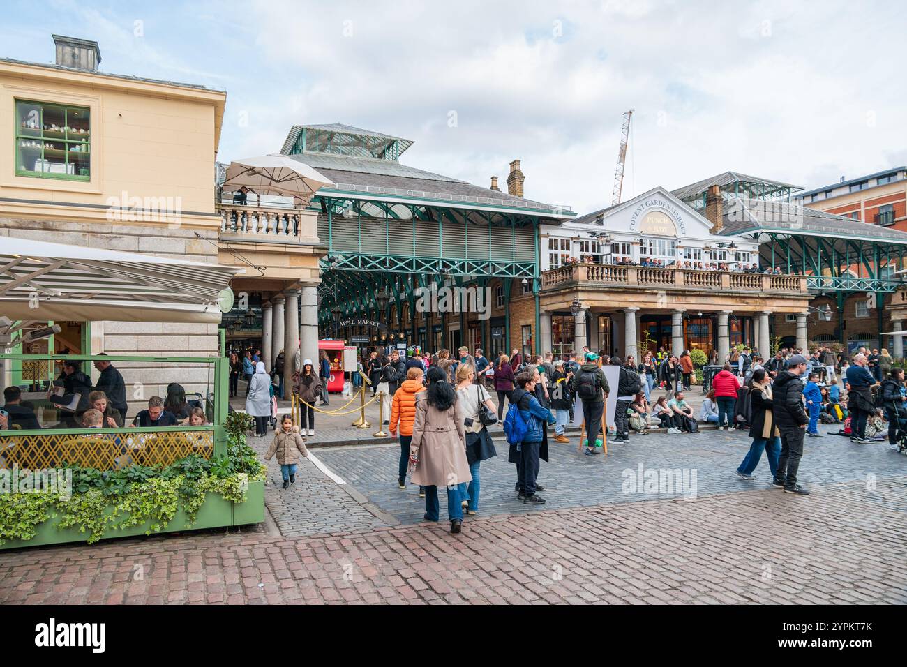 La folla si riunisce presso lo storico colonnato del Covent Garden Market, con lavori in ferro vittoriani e la piazza acciottolata che creano una vibrante atmosfera per lo shopping Foto Stock
