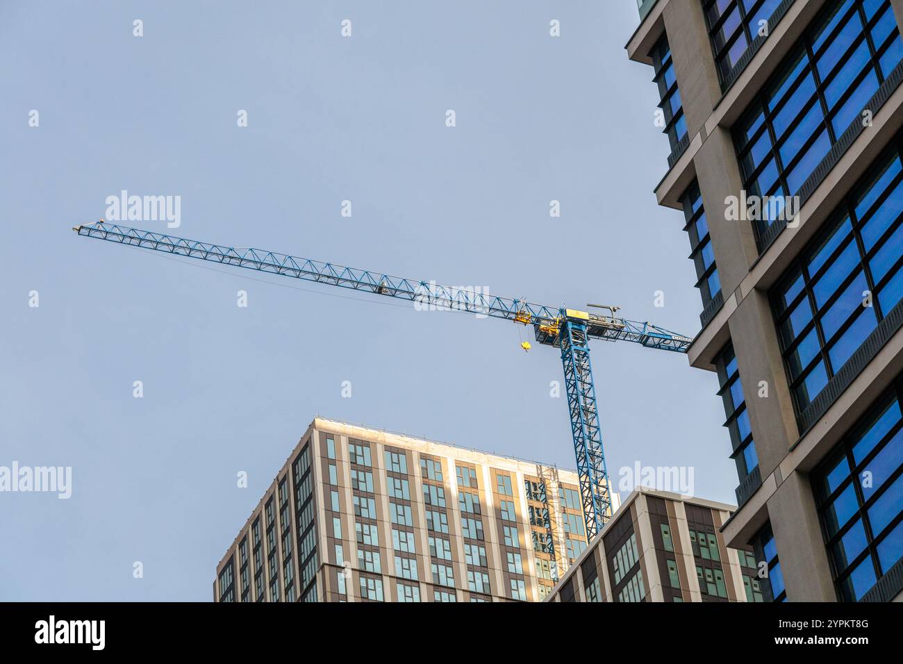 La gru da costruzione sovrasta i moderni edifici residenziali di Canary Wharf, evidenziando lo sviluppo urbano in corso contro il cielo azzurro Foto Stock