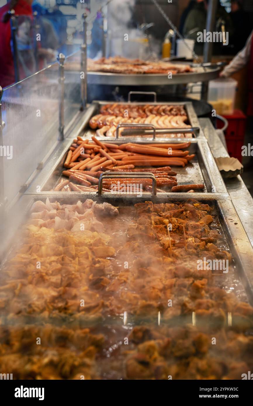 Grande bancarelle di barbecue al mercatino di Natale con varie salsicce calde, spiedini di carne e fumo, cibo di strada stagionale durante un evento natalizio, V Foto Stock