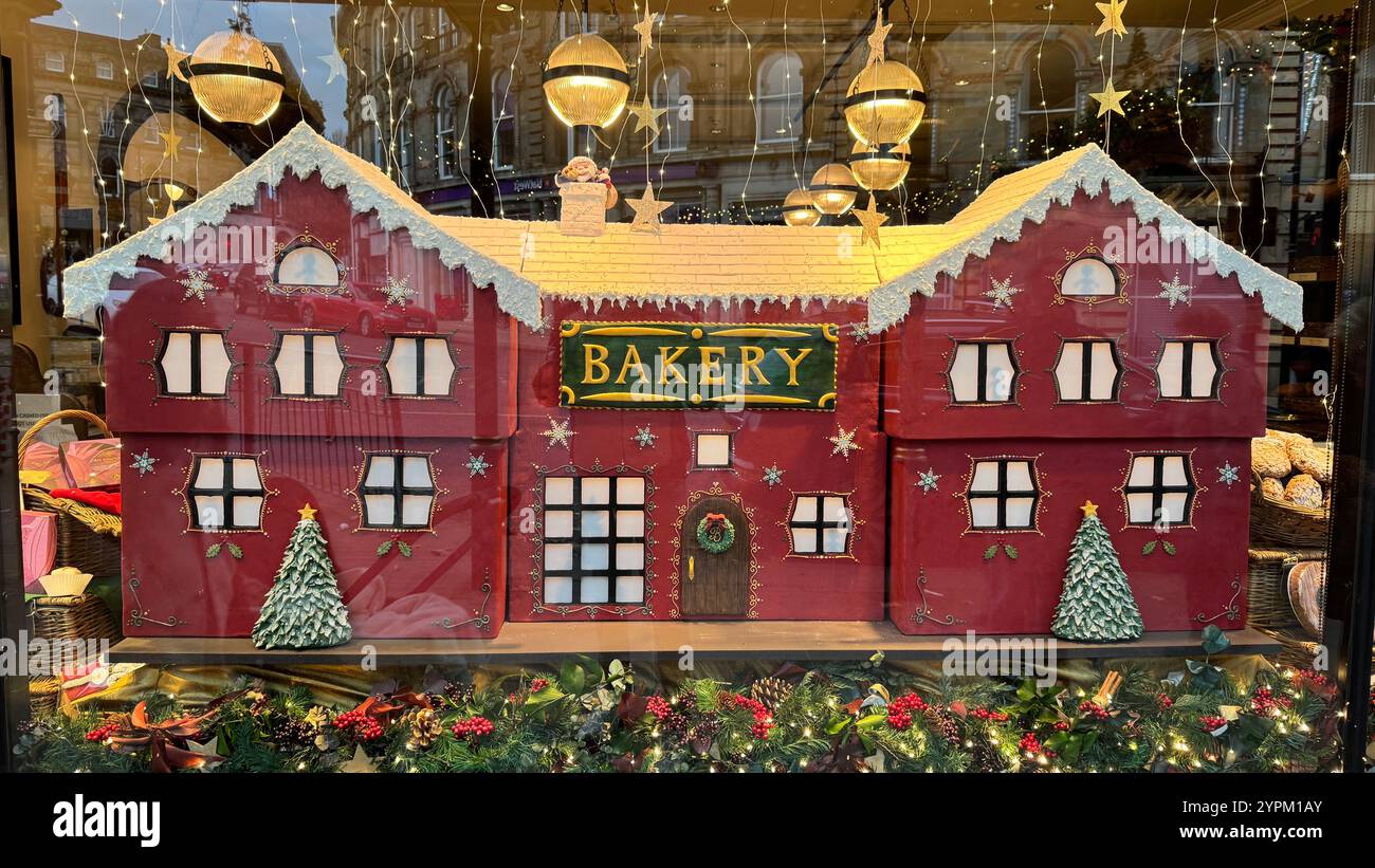 Una replica rossa e festosa di un edificio di panificio domina una vetrina di panificio. Dispone di finestre illuminate, un cartello "Bakery" ed è adornato da neve Foto Stock