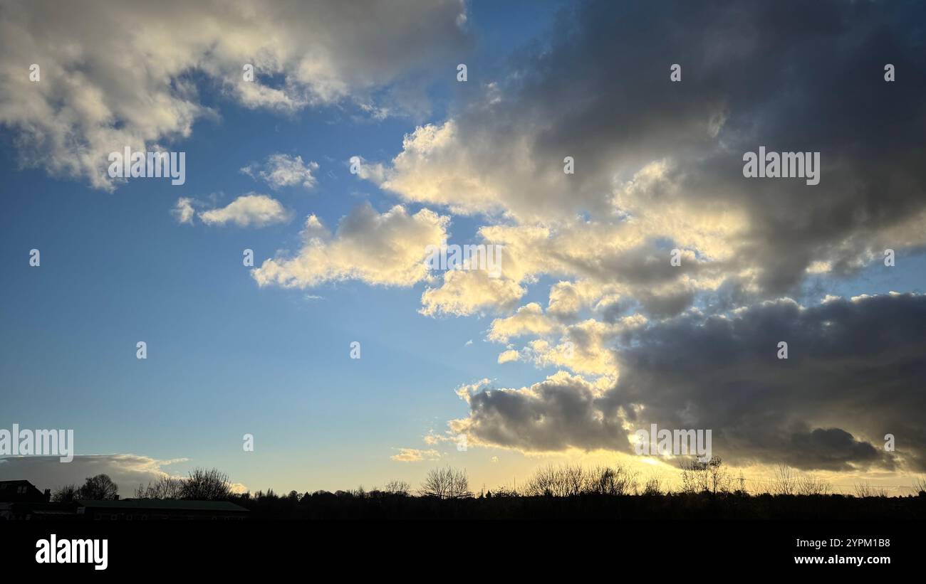 Una vista panoramica di un cielo parzialmente nuvoloso al tramonto. Il cielo è prevalentemente blu con una grande distesa di nuvole grigie scure contrapposte da un giallo luminoso Foto Stock