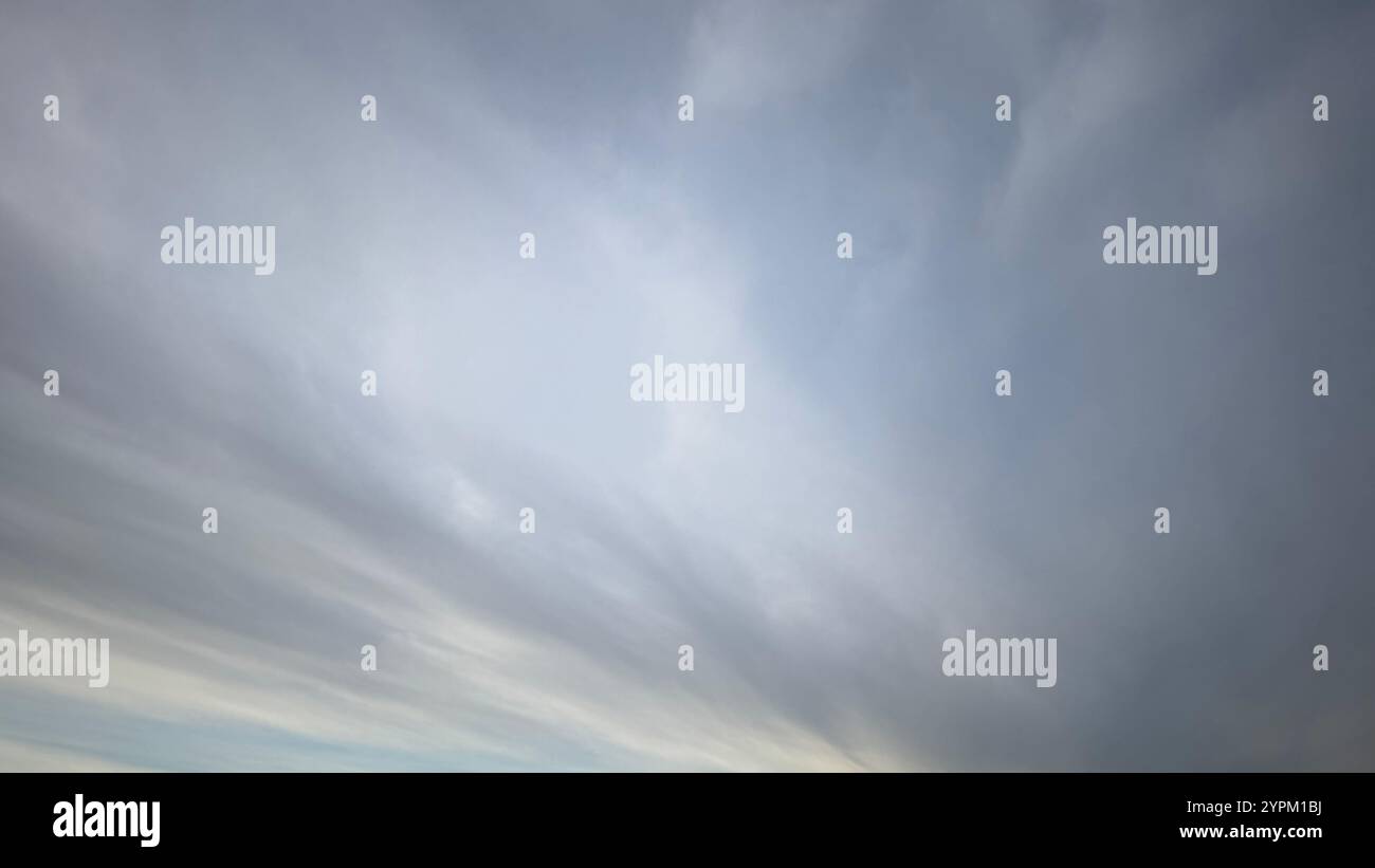 Vista ad angolo basso di un cielo prevalentemente coperto. Le nuvole sono principalmente di colore grigio chiaro e bianco, con un motivo striato e fluido. L'orizzonte è barel Foto Stock