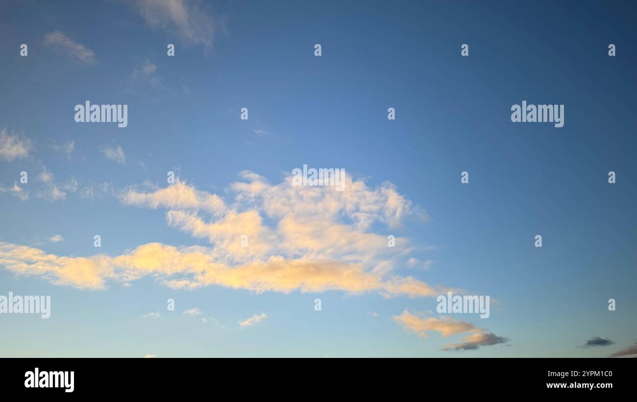 Un cielo blu per lo più limpido con una banda prominente di nuvole cirrus giallo-bianche che si estendono orizzontalmente attraverso la terza parte centrale. Più piccolo, simile cl Foto Stock