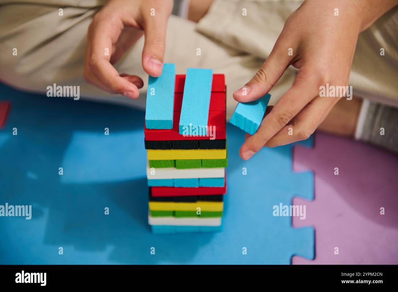 Primo piano di un bambino che impila blocchi di legno colorati su un tappetino in schiuma. L'attività promuove il coordinamento mano-occhio, la creatività e le capacità cognitive. Foto Stock