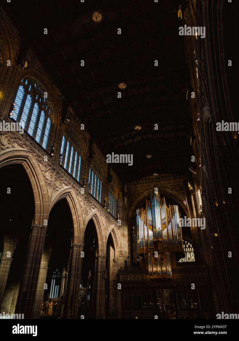 Stupendo interno della cattedrale con archi ornati, vetrate colorate e un maestoso organo a canne con illuminazione bassa Foto Stock