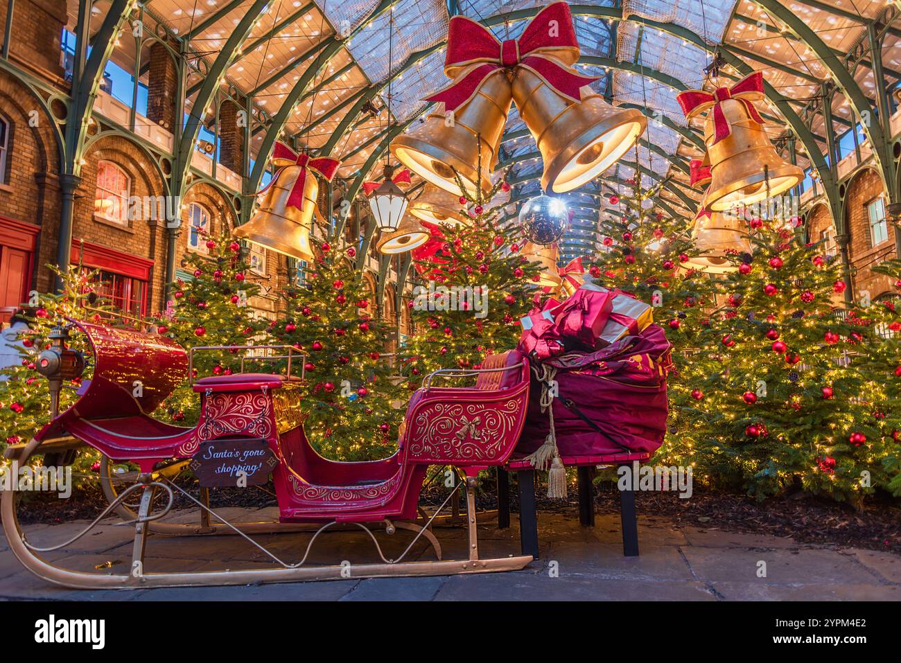 La scena natalizia di Covent Garden presenta una slitta festosa, torreggianti alberi di Natale, campane dorate, luci scintillanti delle fate e vivaci decorazioni a lo Foto Stock