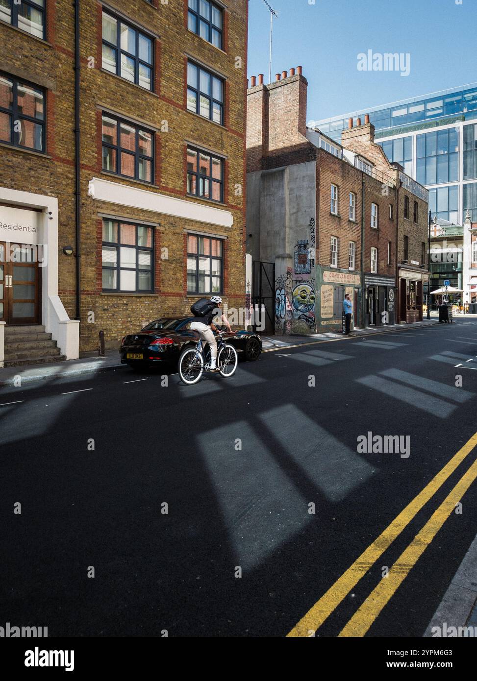 Scena urbana di Londra con un ciclista che passa davanti a edifici in mattoni, graffiti e architettura moderna della città in una giornata di sole Foto Stock