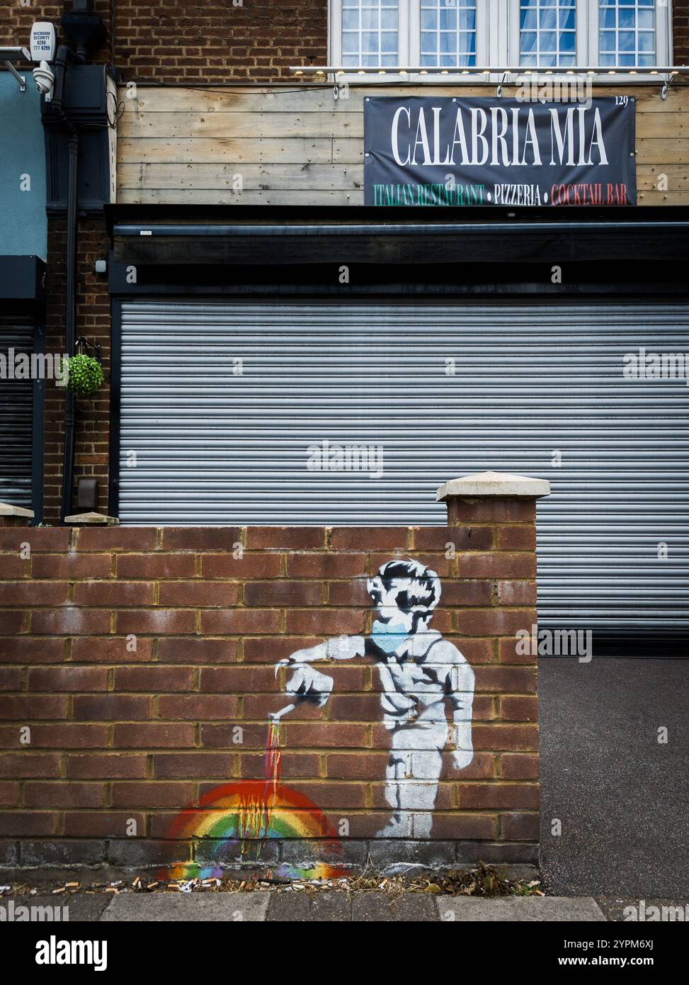 Murale di strada di un bambino che dipinge un arcobaleno su un muro di mattoni fuori da un ristorante italiano con persiane in un ambiente urbano Foto Stock