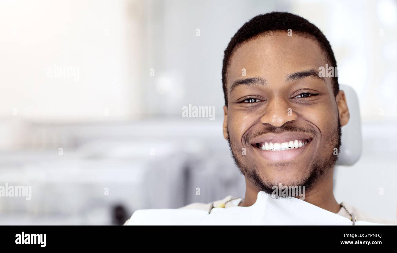 Felice giovane uomo nero seduto in sedia dentista e mostrando il pollice in su Foto Stock