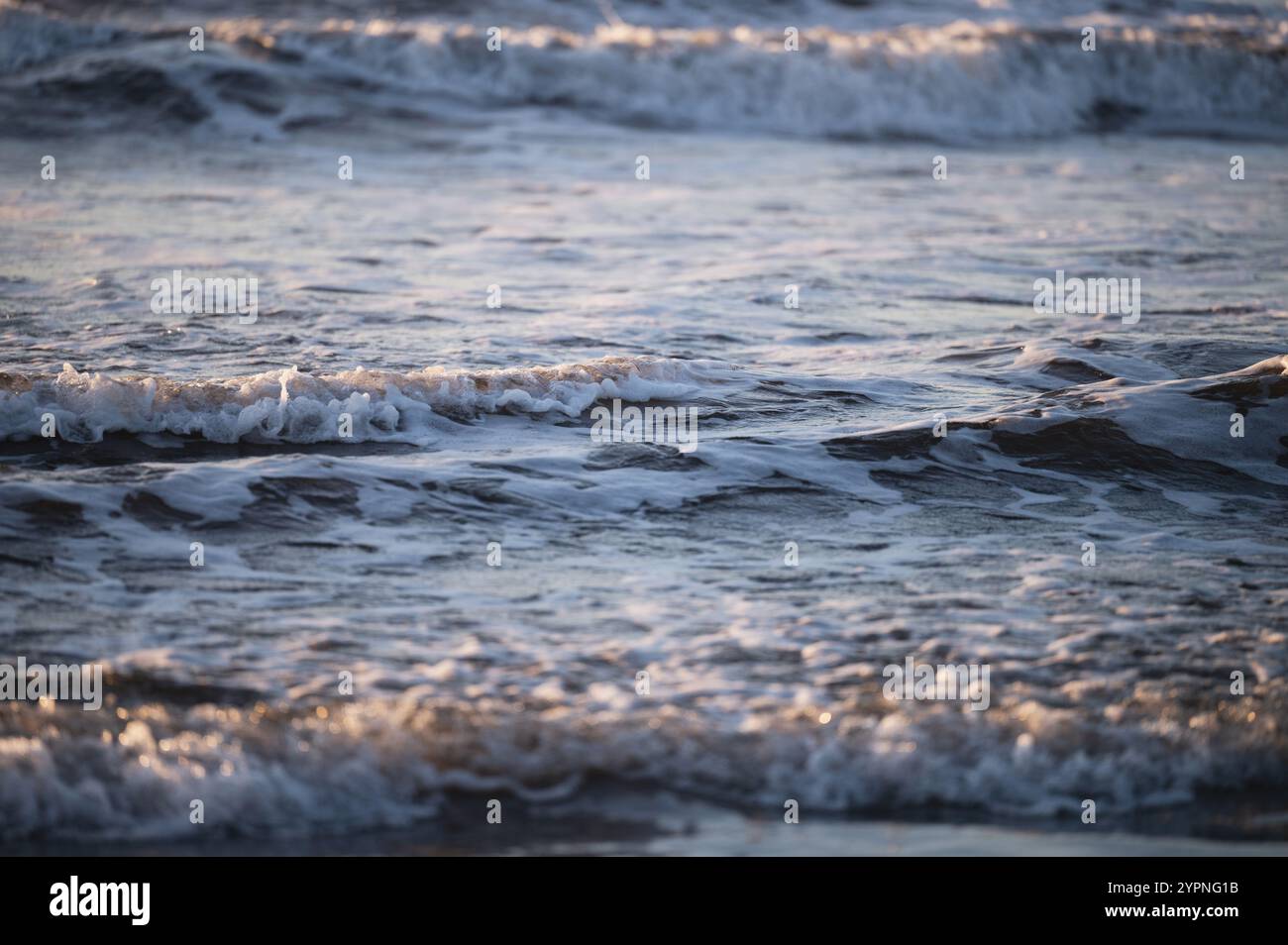 Le calme onde dell'oceano creano un ritmo rilassante mentre la luce del sole si riflette sull'acqua al tramonto. Foto Stock