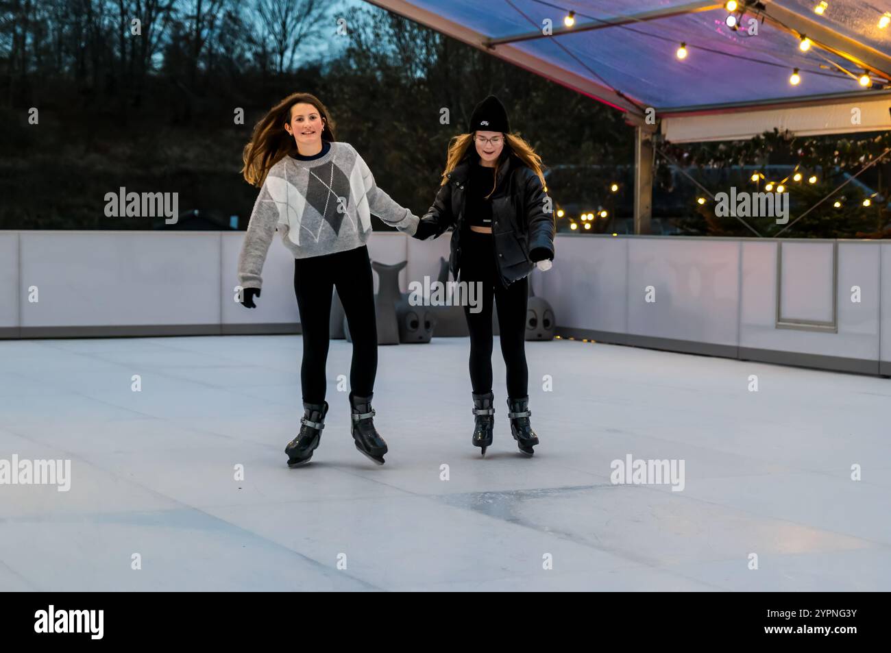 Due ragazze si divertono su una pista di pattinaggio su ghiaccio ecosostenibile, Dalkeith Country Park, Midlothian, Scozia, Regno Unito Foto Stock