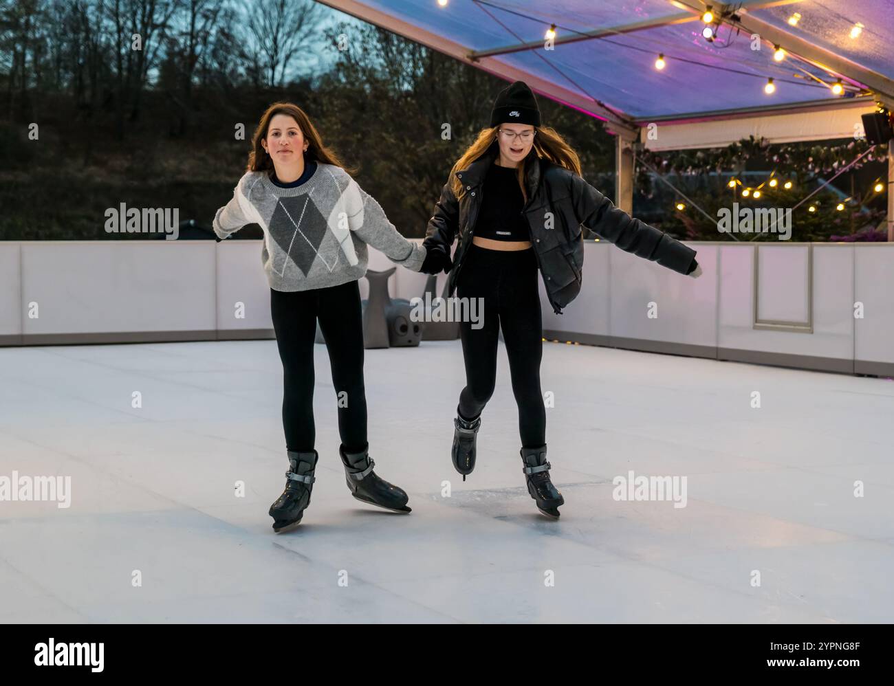 Due ragazze si divertono su una pista di pattinaggio su ghiaccio ecosostenibile, Dalkeith Country Park, Midlothian, Scozia, Regno Unito Foto Stock