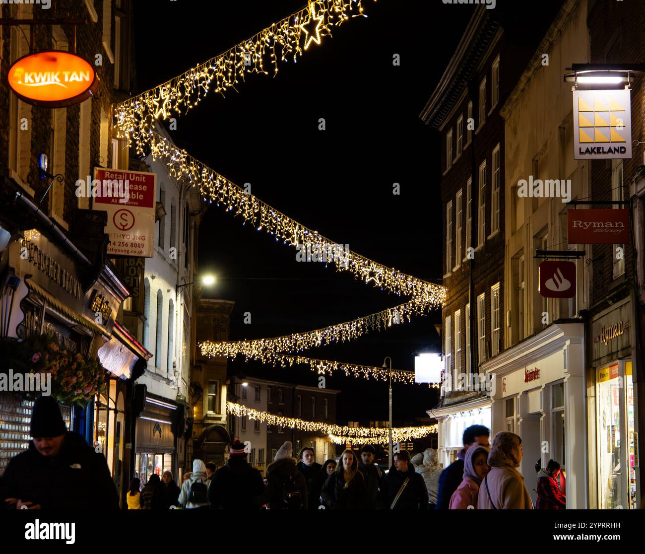 Una strada trafficata adornata da luci a corda e decorazioni natalizie mentre la gente passeggia per l'affascinante scena serale York 2024 Foto Stock