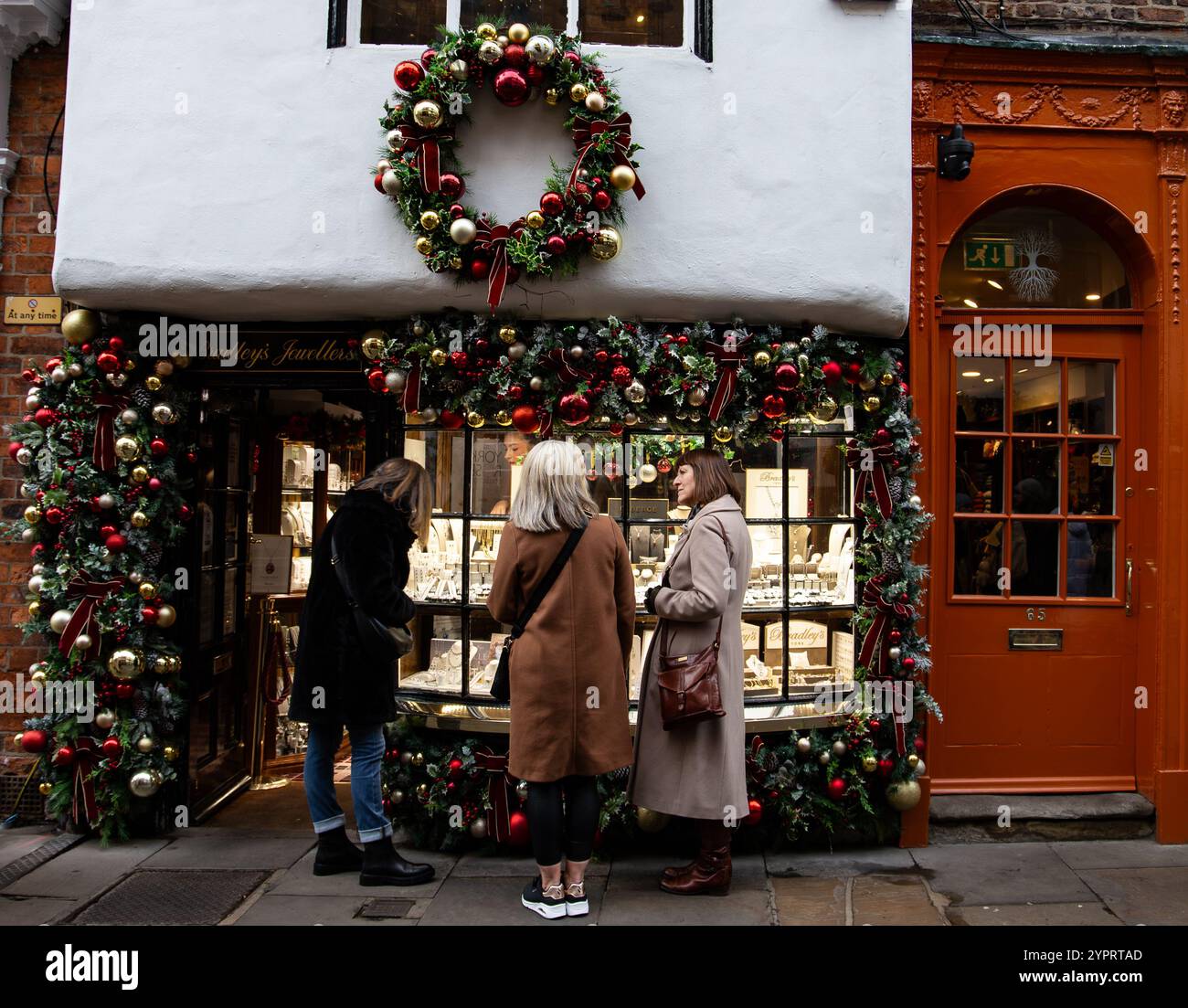 Tre persone si trovano all'esterno di un negozio di gioielli decorato che espone ornamenti natalizi in un ambiente a tema natalizio a York, Regno Unito Foto Stock
